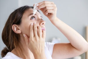 Young woman putting in eye drops to combat dry eye condition